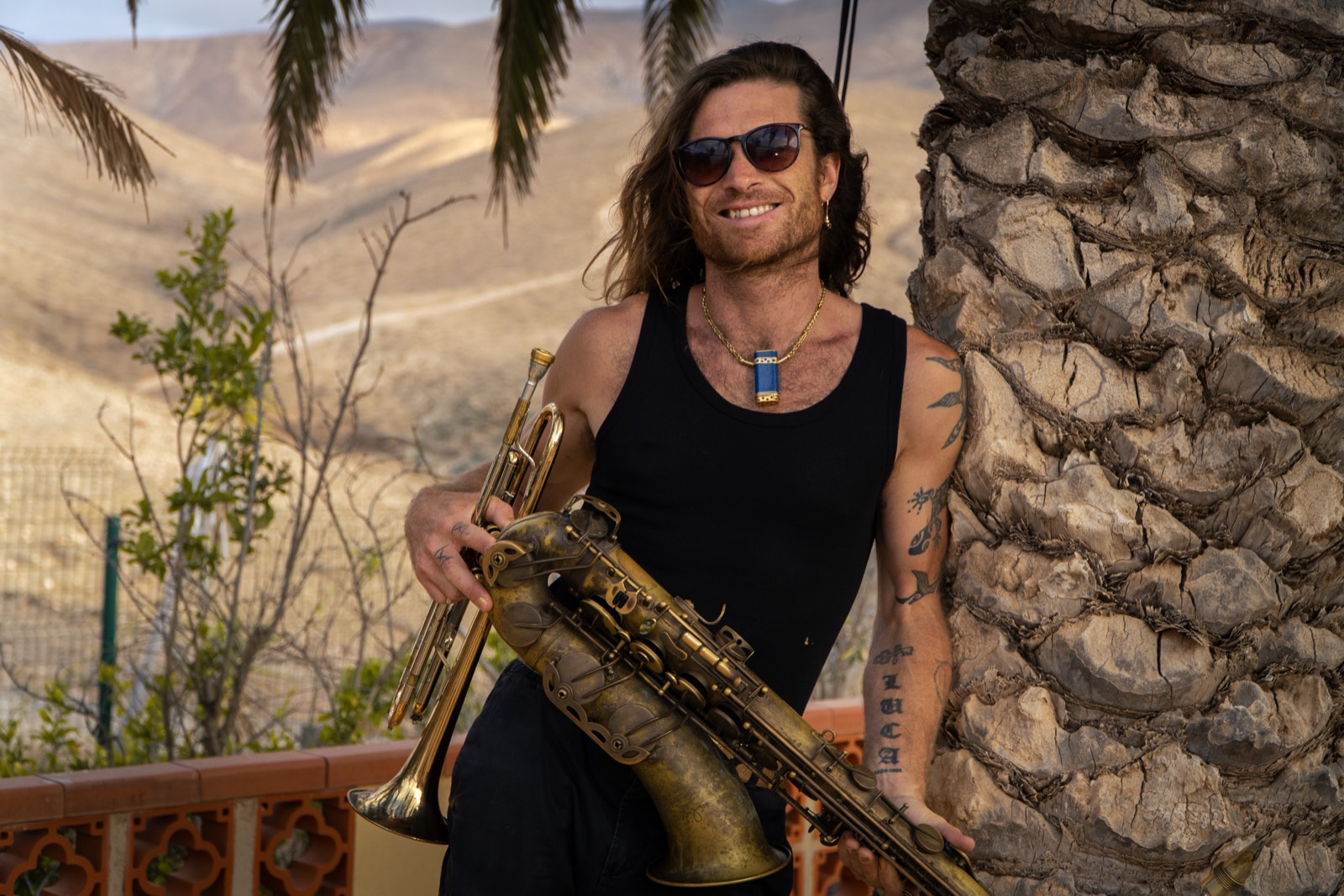 Luca Simonelli outdoors in Fuerteventura, holding a trumpet and a saxophone