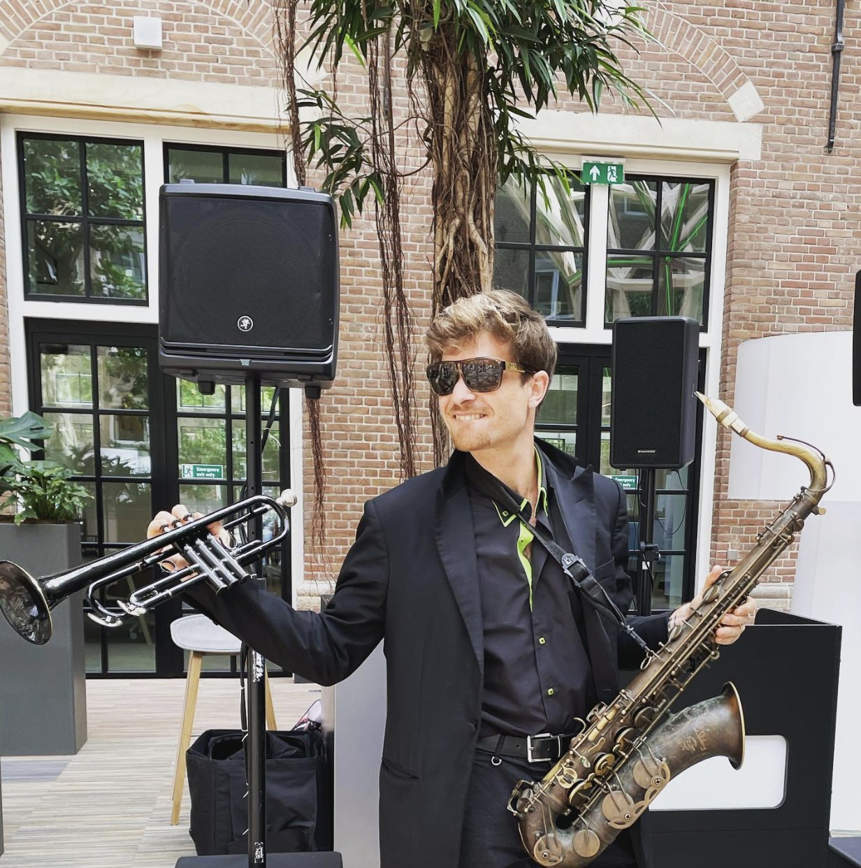 Luca Simonelli performing outdoors, holding trumpet and saxophone